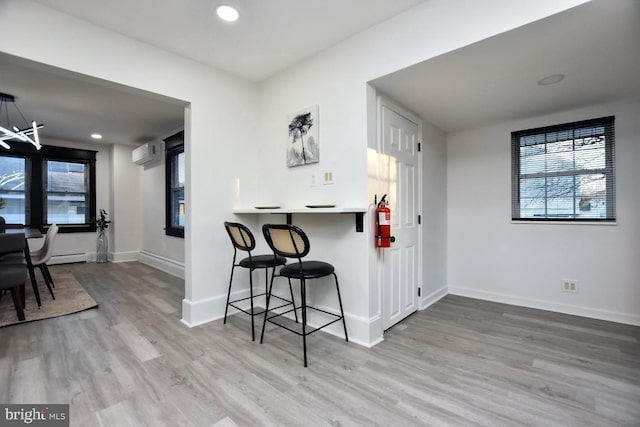 kitchen featuring an AC wall unit, a kitchen breakfast bar, wood finished floors, recessed lighting, and baseboards