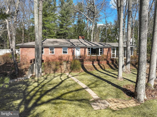 single story home featuring brick siding, a chimney, and a front yard