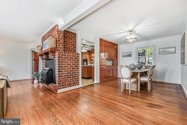 dining room with baseboards, a wood stove, light wood-style flooring, ceiling fan, and ornamental molding