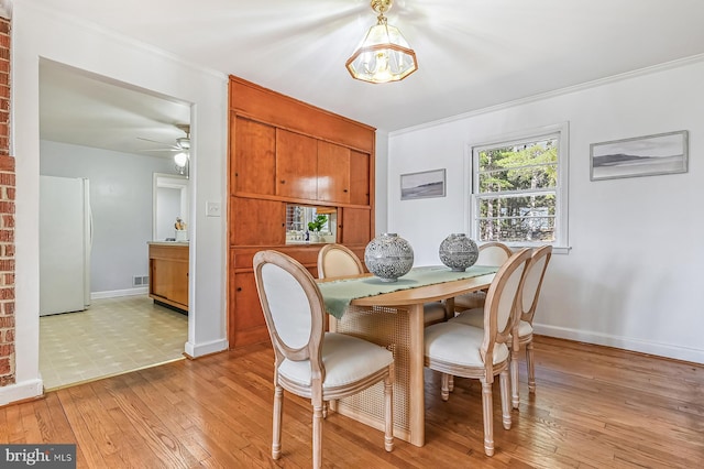 dining room with light wood-type flooring, visible vents, ornamental molding, a ceiling fan, and baseboards