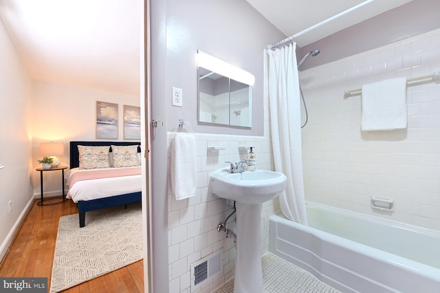 bathroom featuring wood finished floors, visible vents, shower / bath combo, tile walls, and connected bathroom