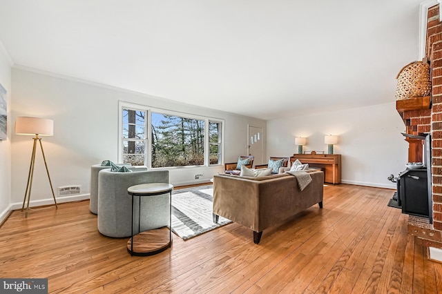 living area featuring visible vents, baseboards, ornamental molding, a fireplace, and light wood-style floors