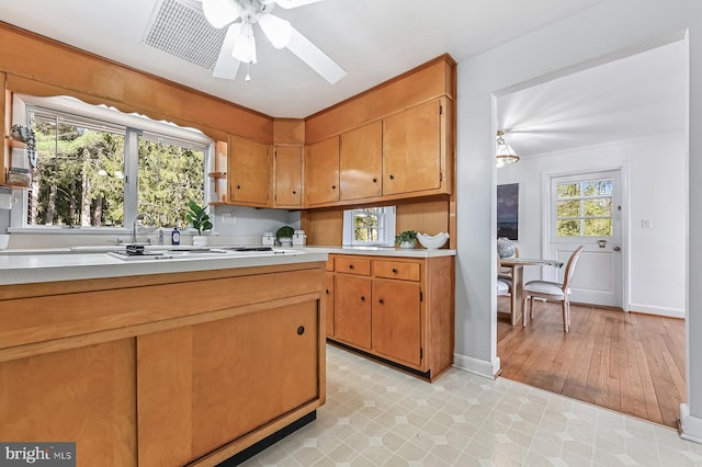 kitchen with a sink, brown cabinetry, light countertops, baseboards, and ceiling fan