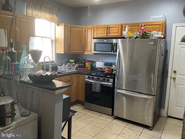 kitchen with a sink, dark countertops, stainless steel appliances, a peninsula, and light tile patterned floors