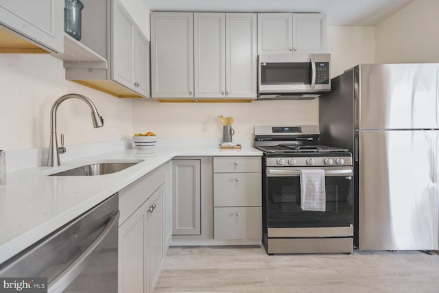 kitchen with appliances with stainless steel finishes, light wood-type flooring, light countertops, and a sink