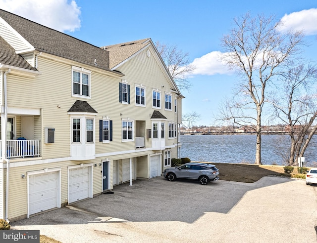 exterior space featuring a water view, driveway, roof with shingles, and an attached garage