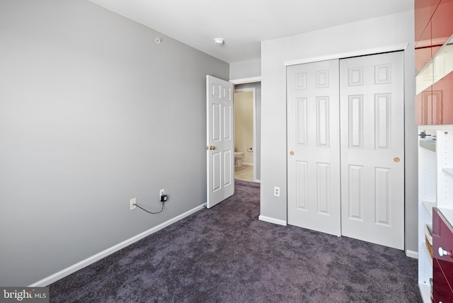 unfurnished bedroom featuring a closet, baseboards, and dark carpet