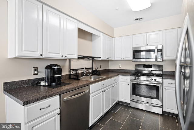 kitchen featuring visible vents, a sink, appliances with stainless steel finishes, white cabinetry, and dark countertops