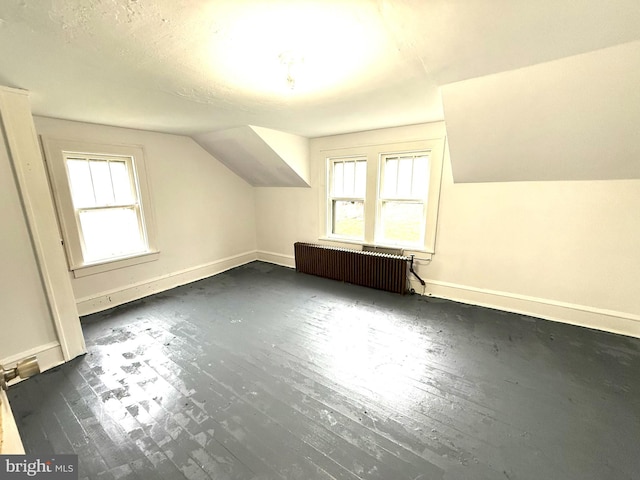 additional living space with dark wood-style flooring, baseboards, vaulted ceiling, and radiator