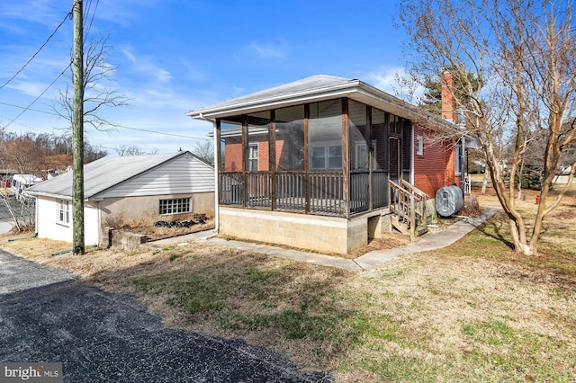 back of property featuring an outdoor structure, a chimney, a yard, and a sunroom