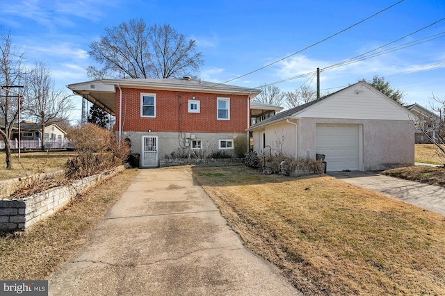 rear view of property with brick siding, concrete driveway, a garage, a yard, and an outbuilding