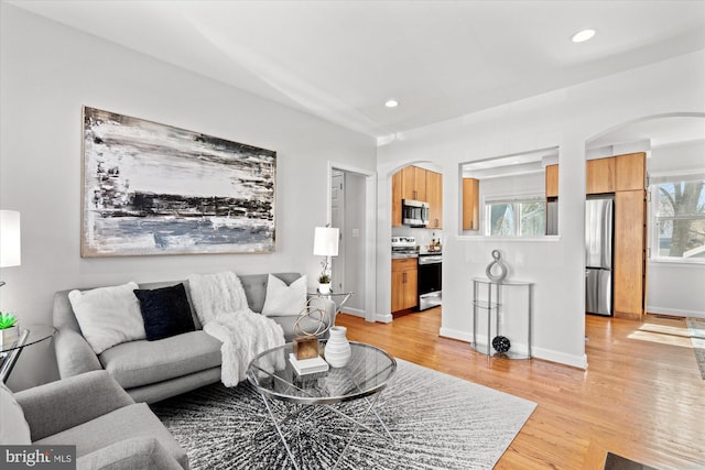 living room with arched walkways, recessed lighting, light wood-type flooring, and baseboards