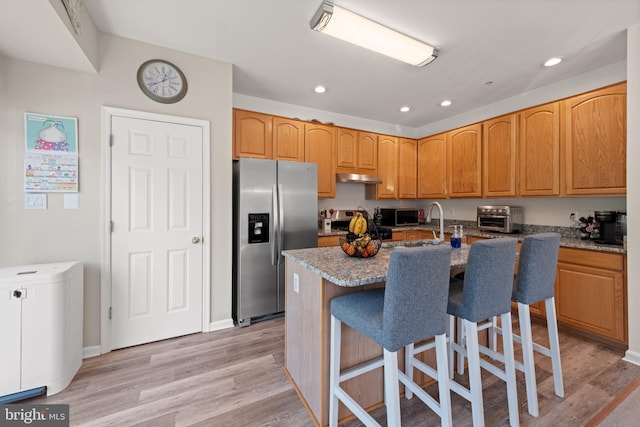 kitchen featuring a center island with sink, a toaster, under cabinet range hood, light wood-style floors, and stainless steel appliances