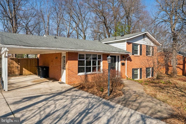 split level home featuring brick siding, concrete driveway, fence, and a carport