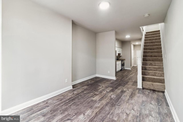 unfurnished living room featuring dark wood-type flooring, stairway, and baseboards