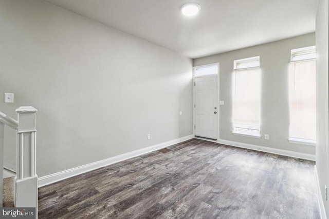 empty room with a wealth of natural light, baseboards, and dark wood-style flooring