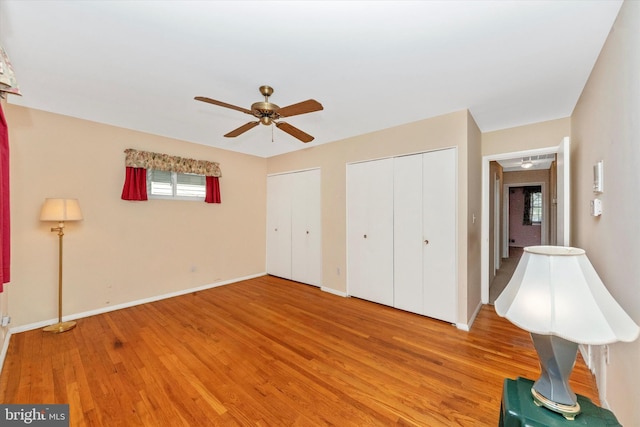 unfurnished bedroom featuring baseboards, ceiling fan, two closets, and light wood-style floors