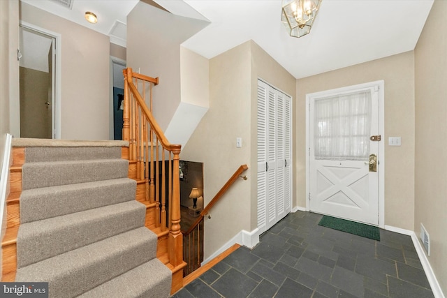 entrance foyer featuring visible vents, baseboards, an inviting chandelier, stairs, and stone finish floor