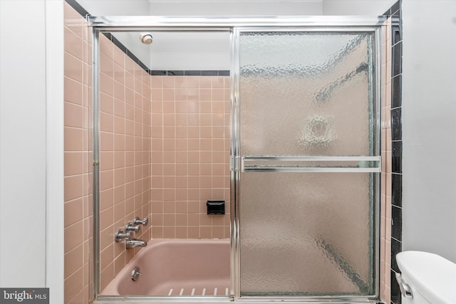 bathroom featuring toilet and shower / bath combination with glass door