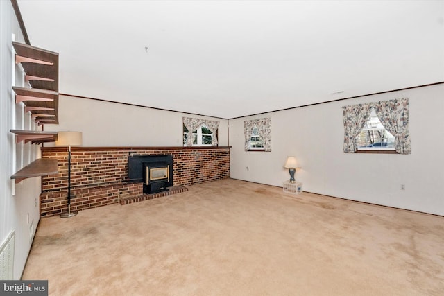 unfurnished living room with a wood stove, brick wall, carpet, and a wealth of natural light