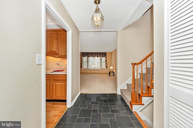 entrance foyer with stairway, stone finish floor, baseboards, and dark colored carpet