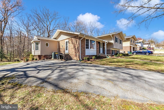 view of side of property featuring aphalt driveway, a lawn, and brick siding