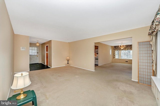 unfurnished living room featuring a chandelier, baseboards, and carpet