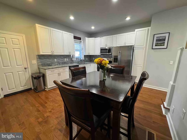 kitchen with stainless steel appliances, dark wood-type flooring, decorative backsplash, and white cabinetry