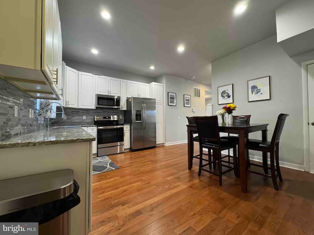 kitchen with light wood-type flooring, a sink, tasteful backsplash, white cabinetry, and stainless steel appliances