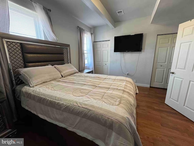 bedroom with visible vents, beam ceiling, baseboards, and wood finished floors