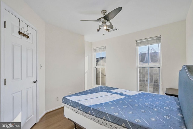 bedroom featuring a ceiling fan, wood finished floors, visible vents, and baseboards