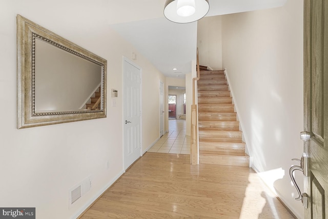 hall with visible vents, baseboards, wood finished floors, and stairway