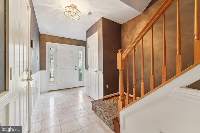 foyer entrance featuring a decorative wall, a wainscoted wall, stairs, and light tile patterned floors