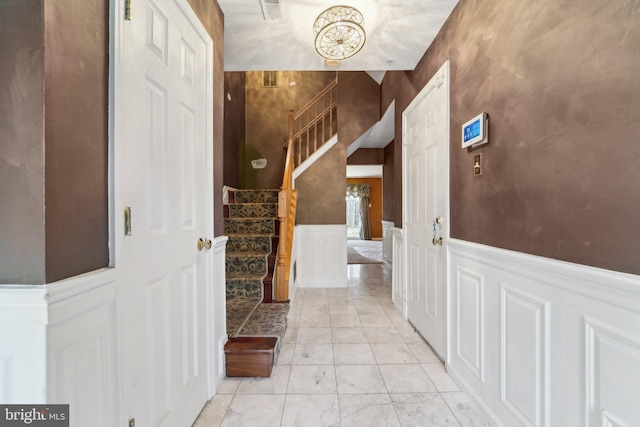 foyer entrance featuring visible vents, wainscoting, stairs, and a decorative wall