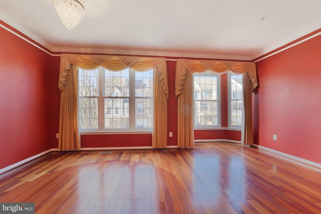 empty room featuring visible vents, ornamental molding, wood finished floors, an inviting chandelier, and baseboards