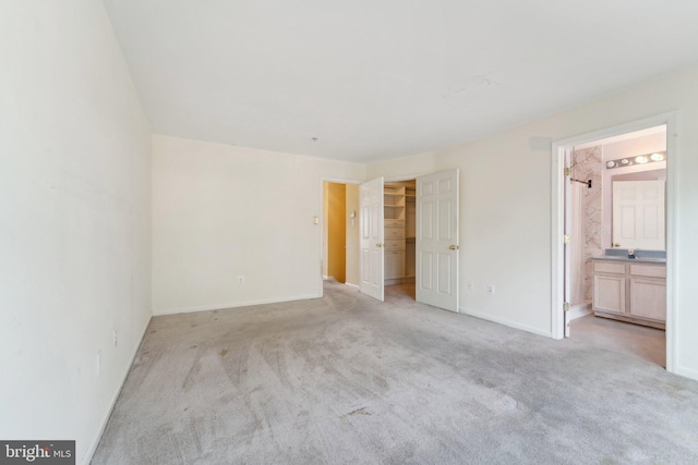 unfurnished bedroom featuring baseboards, a sink, a spacious closet, light carpet, and connected bathroom