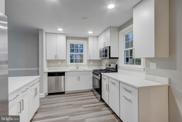 kitchen with light stone counters, appliances with stainless steel finishes, light wood-style floors, white cabinetry, and a sink