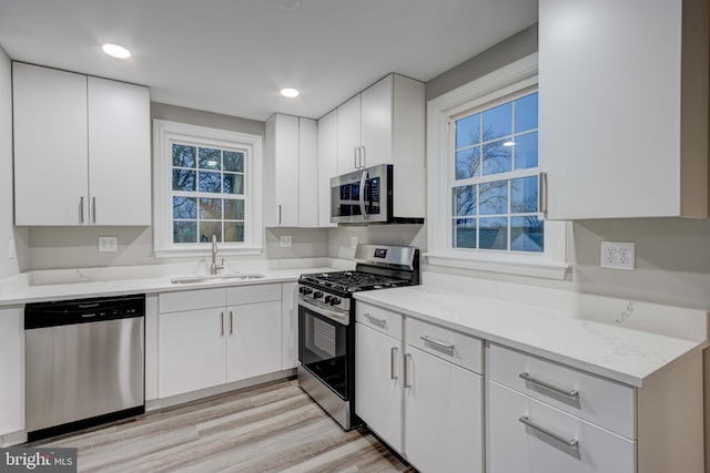 kitchen featuring white cabinets, appliances with stainless steel finishes, light wood-style flooring, and a sink