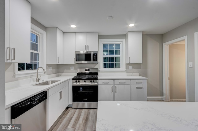 kitchen featuring recessed lighting, appliances with stainless steel finishes, light wood-style flooring, white cabinets, and a sink