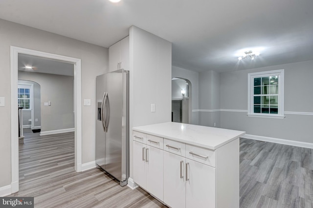 kitchen with light wood finished floors, stainless steel fridge with ice dispenser, a peninsula, arched walkways, and white cabinets