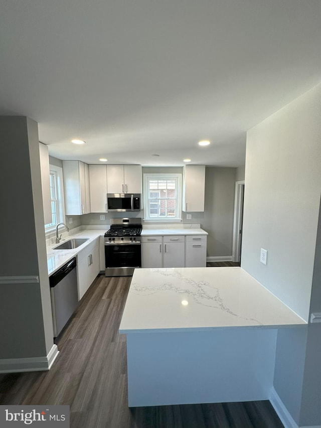 kitchen featuring light stone counters, dark wood finished floors, a sink, stainless steel appliances, and white cabinets