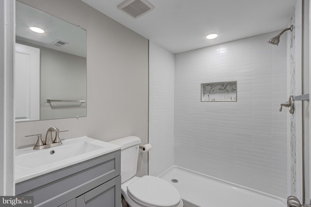 full bath featuring a tile shower, visible vents, toilet, and vanity