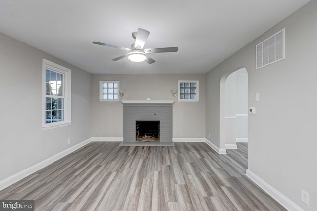 unfurnished living room featuring a ceiling fan, wood finished floors, visible vents, baseboards, and a brick fireplace