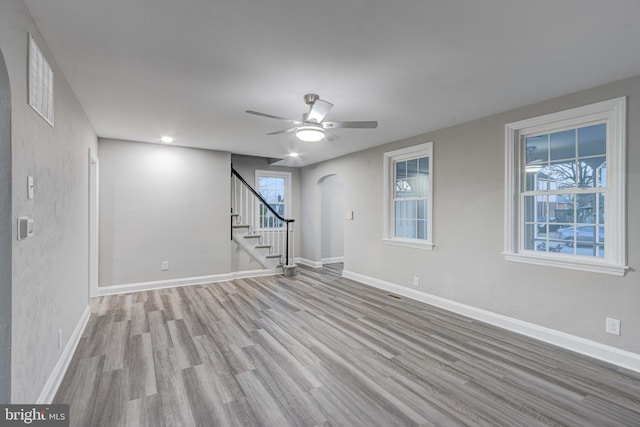 unfurnished living room featuring baseboards, a ceiling fan, wood finished floors, and stairs