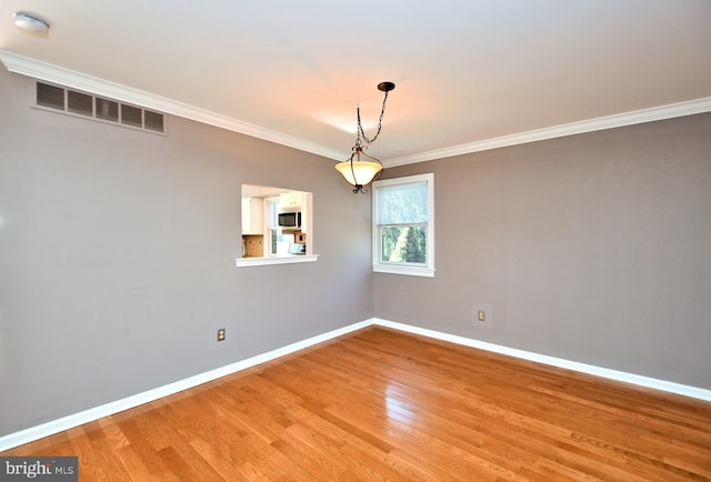 empty room featuring baseboards, light wood-style floors, visible vents, and ornamental molding