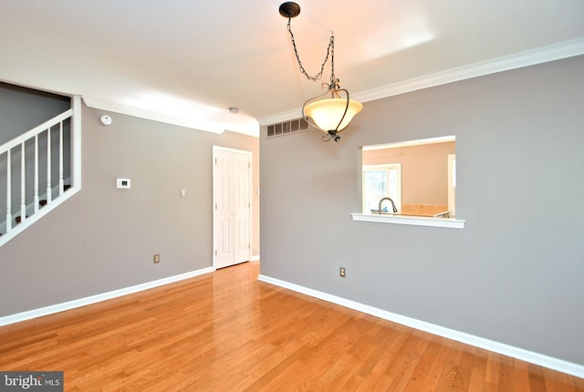 unfurnished room with stairway, wood finished floors, visible vents, and ornamental molding