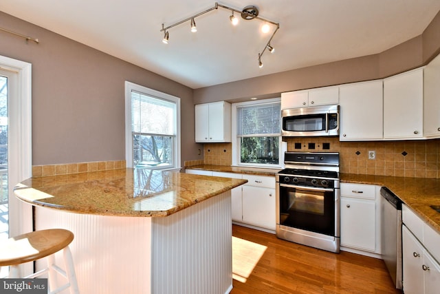 kitchen with light wood-style flooring, tasteful backsplash, stainless steel appliances, a peninsula, and white cabinets