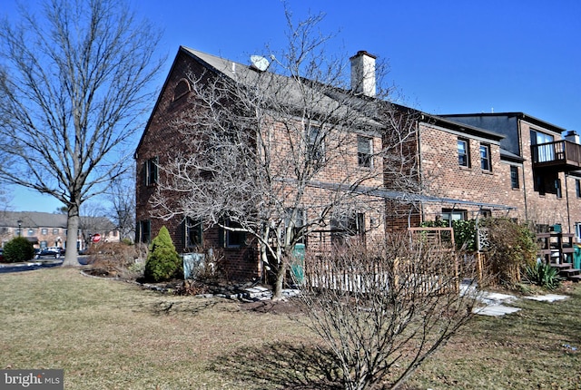 view of property exterior with brick siding, a lawn, and a chimney