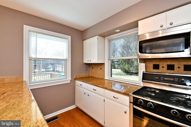 kitchen with visible vents, decorative backsplash, black range with gas cooktop, stainless steel microwave, and a wealth of natural light