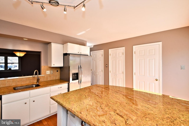 kitchen with light stone countertops, decorative backsplash, stainless steel refrigerator with ice dispenser, white cabinets, and a sink